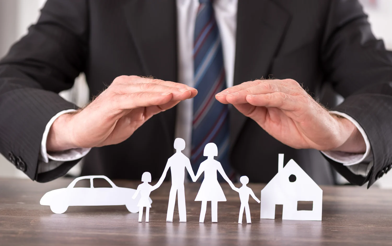 A man in formal attire holds cutouts of a family and a car, illustrating the concept of insurance brokerage services.